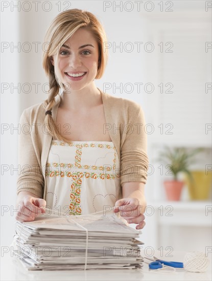 Portrait of young woman recycling newspaper in kitchen. Photographe : Daniel Grill