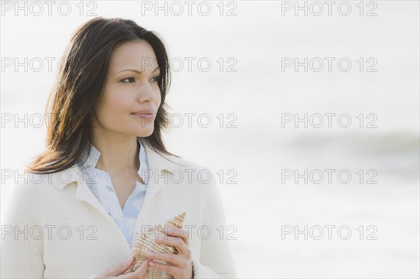 Woman holding shell by sea. Photographe : PT Images