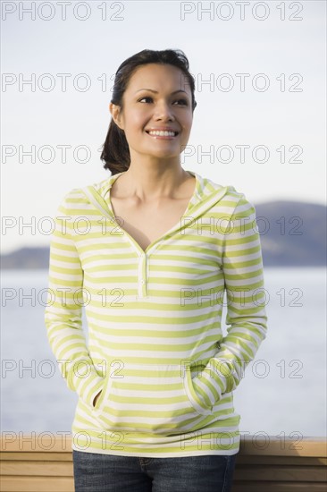 Woman standing at waterfront, smiling. Photographe : PT Images