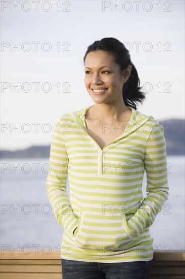 Woman standing at waterfront, smiling. Photographe : PT Images