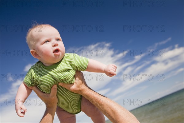 Senior man lifting baby in air, Beaver Island, Michigan, USA. Photographe : Shawn O'Connor