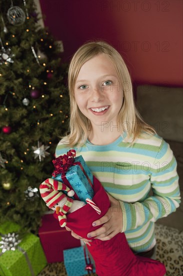 Teenage girl (13-15) holding Christmas presents in Christmas stocking, portrait. Photographe : Sarah M. Golonka