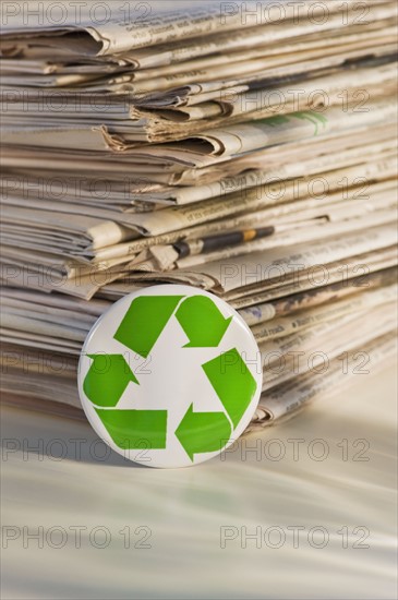 Recycling sign by pile of newspapers, studio shot. Photographe : Daniel Grill