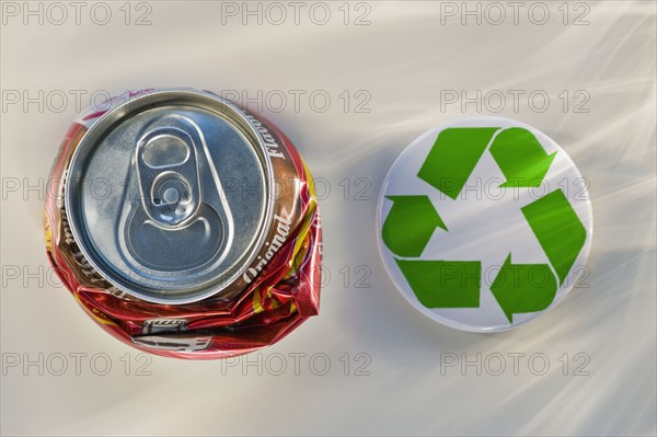 Recycling sign beside crushed can, studio shot. Photographe : Daniel Grill