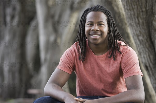 Portrait of teenage boy (16-17) with dreadlocks, sitting in park. Photographe : PT Images