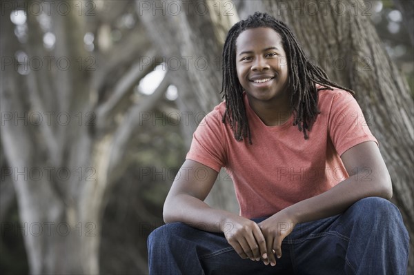 Portrait of teenage boy (16-17) with dreadlocks, sitting in park. Photographe : PT Images