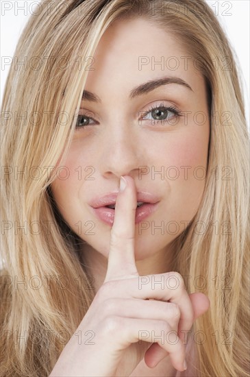 Studio portrait of young woman with finger to lips. Photographe : Daniel Grill