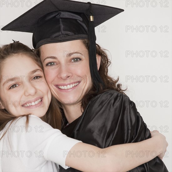 Daughter (10-12 years) embracing mother after her graduation, smiling, portrait. Photographe : Jamie Grill