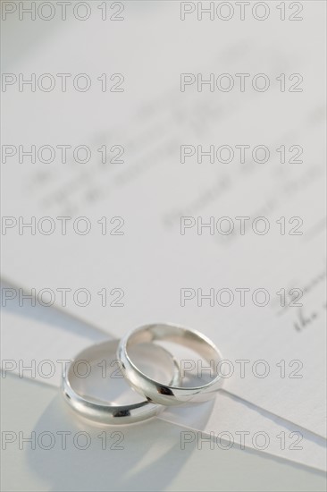 Two wedding rings on marriage certificate, studio shot. Photographe : Jamie Grill