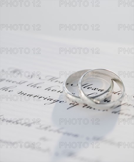 Two wedding rings on marriage certificate, studio shot. Photographe : Jamie Grill