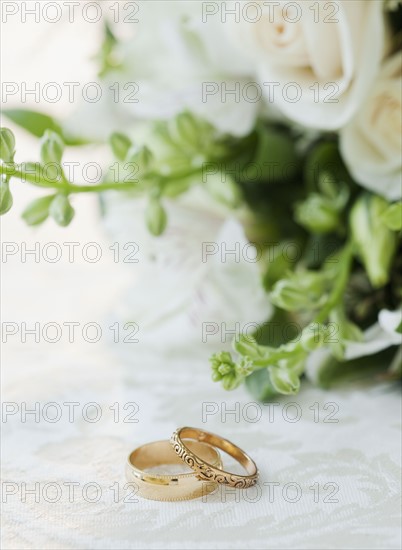 Two wedding rings by bouquet of flowers, studio shot. Photographe : Jamie Grill