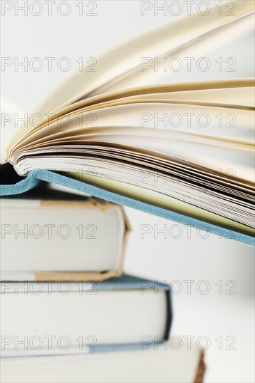 Pile of books with one open, studio shot. Photographe : Jamie Grill