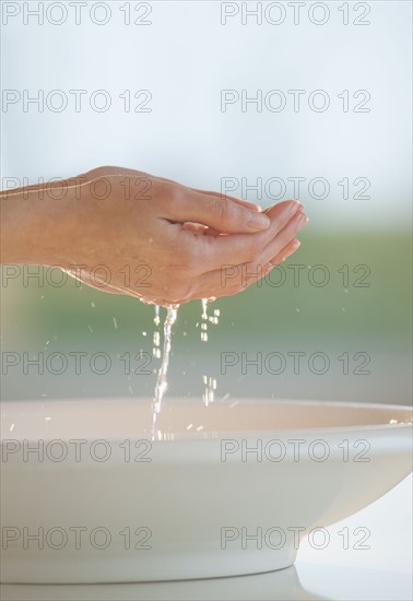 Water dripping from cupped hands over bowl.