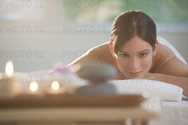 Mid-adult woman lying on massage table with candles and rocks in foreground.