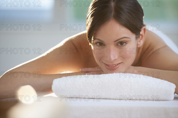 Mid-adult woman lying on massage table with candle in foreground.