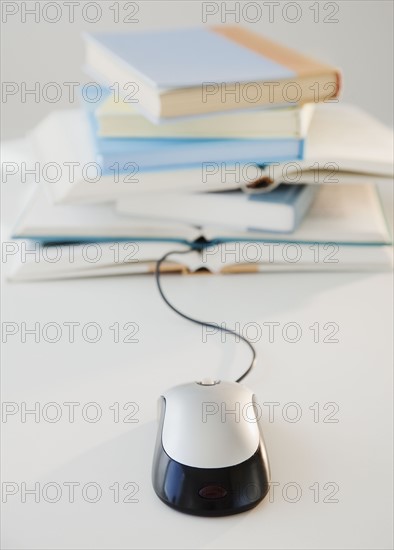 Computer mouse near pile of books, studio shot. Photographe : Jamie Grill