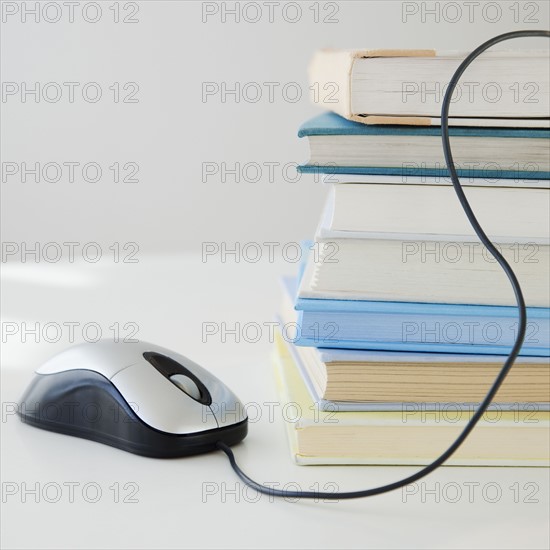 Computer mouse near pile of books, studio shot. Photographe : Jamie Grill