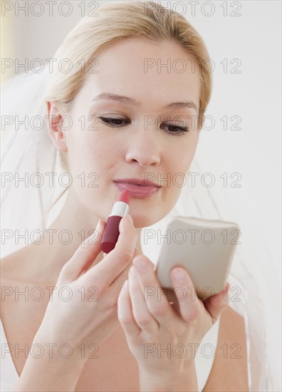 Young bride applying lipstick. Photographe : Jamie Grill