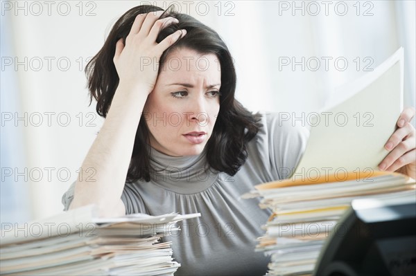 Stressed business woman reading paperwork in office.