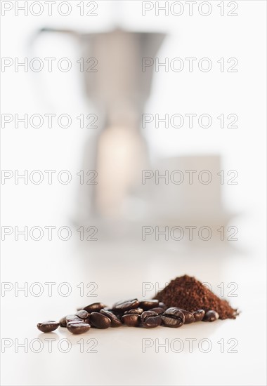 Heap of coffee beans with coffee cups in background.