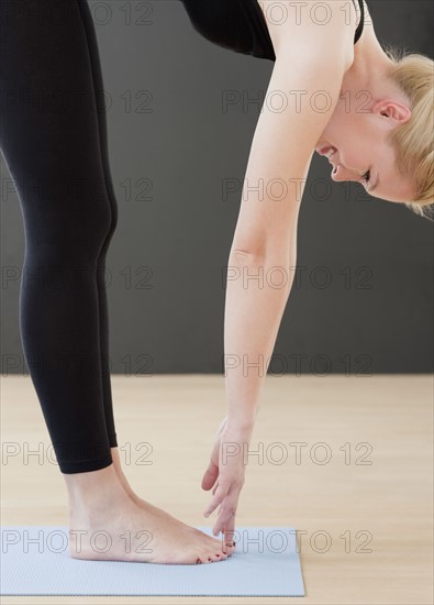 Young woman bending down while doing yoga. Photographe : Jamie Grill