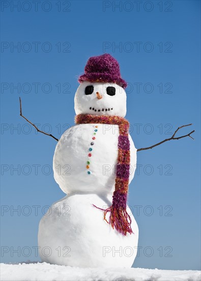 Snowman wearing hat and scarf, clear sky in background.