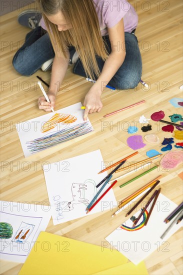 Girl (10-12) sitting on floor and drawing pictures. Photographe : Sarah M. Golonka