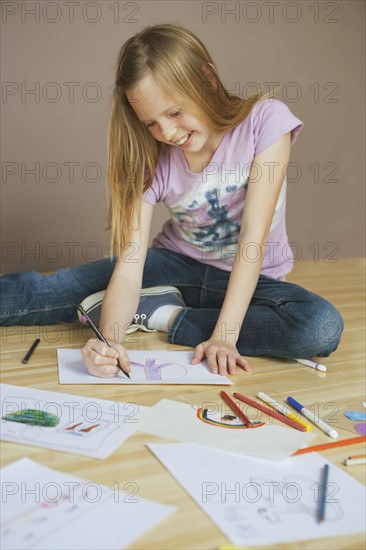 Girl (10-12) sitting on floor and drawing pictures. Photographe : Sarah M. Golonka