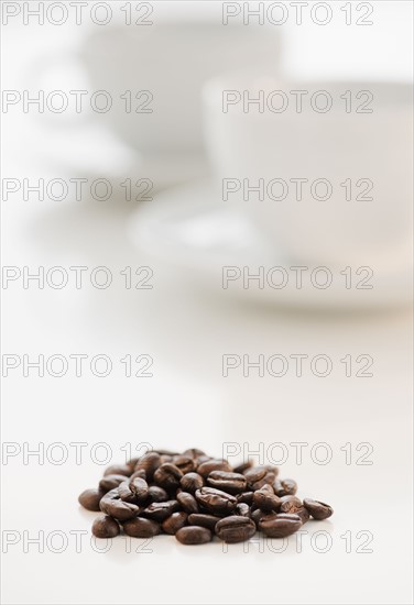 Heap of coffee beans with coffee cups in background.
