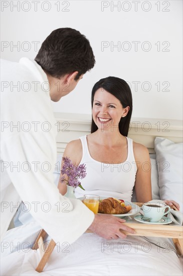 A man bringing a woman breakfast in bed.