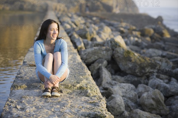 A woman sitting on a stone wall by water