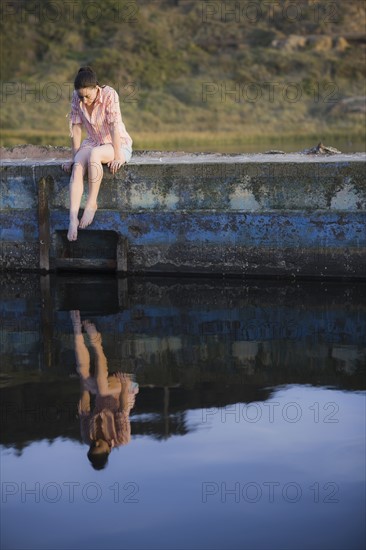 A woman sitting on a stone wall by water