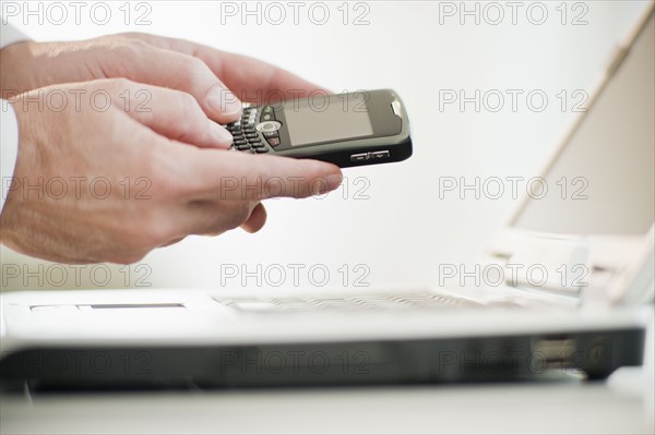 Hands holding a personal digital assistant over a laptop.