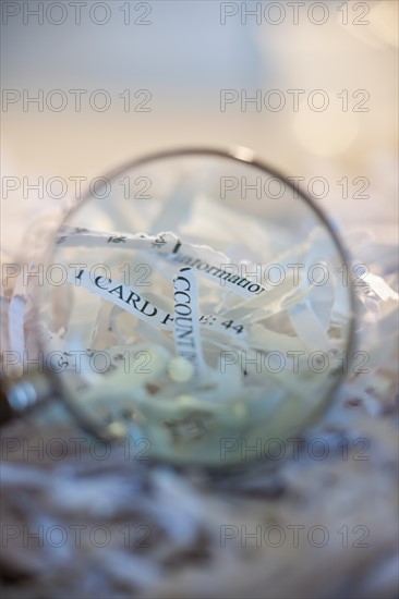 Confidential paperwork shredded under a magnifying glass.