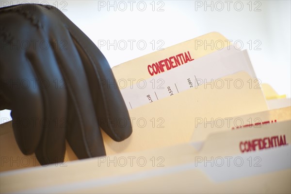 A gloved hand taking confidential files.