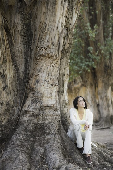 A woman outdoors sitting by a large tree