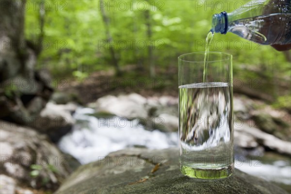 Bottled water being poured into a glass in the woods
