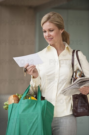 Woman with grocery bags looking at mail.