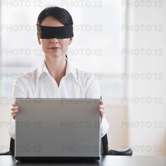 Businesswoman using laptop while blindfolded.
