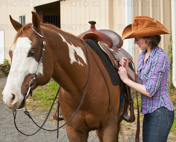 Woman putting saddle on horse.