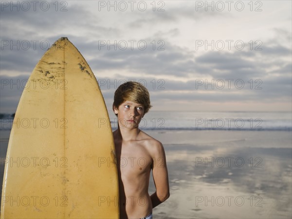 Boy standing beside surfboard