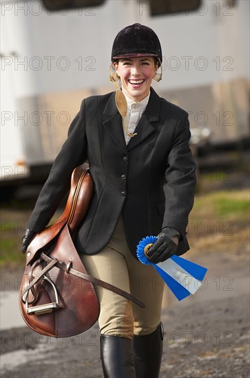 Jockey walking with saddle and ribbon.