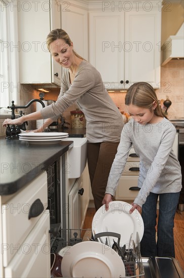 Mother and daughter loading dishwasher.