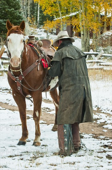 Man putting saddle on horse.