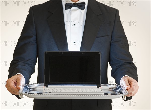 Butler holding laptop on tray.