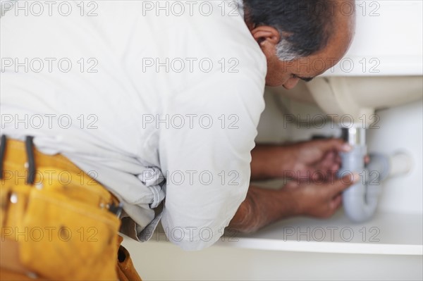 Plumber fixing sink. Photographer: momentimages