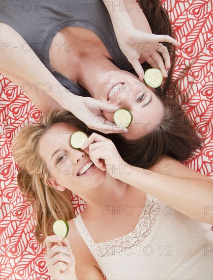 Friends putting cucumber slices on eyes. Photographer: Jamie Grill