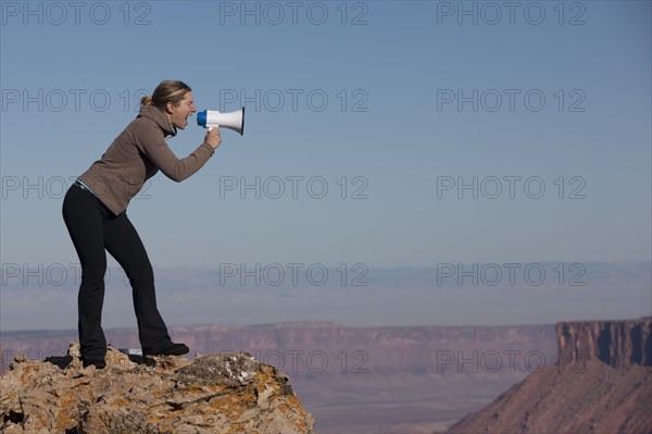 Woman yelling into megaphone at top of canyon. Photographer: Dan Bannister
