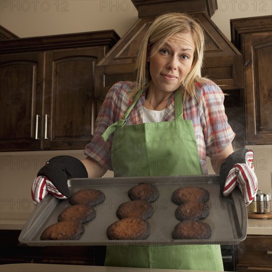 Woman holding tray of burnt cookies. Photographer: Mike Kemp