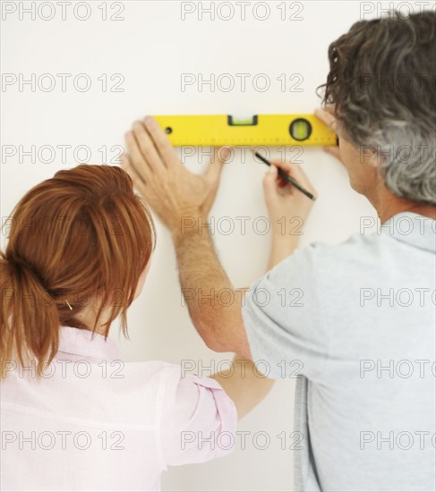 Couple marking a straight line on wall. Photographer: momentimages